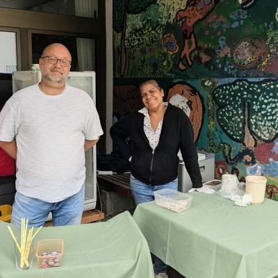 Ein Mann und eine Frau stehen beim Getränkeverkauf und lachen in die Kamera