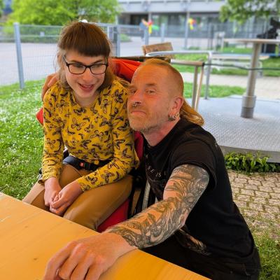 Ein Mann und ein Mädchen im Rollstuhl lachen in die Kamera
