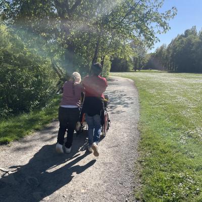 Zwei Menschen schieben einen Rollstuhl, man sieht sie von hinten