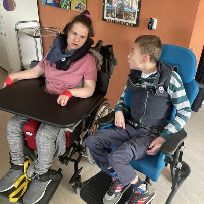 Eine junge Frau und ein Junge sind nebeneinander, beide sitzen im Rollstuhl.