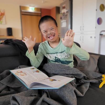 Ein Junge, der gemütlich zugedeckt auf dem Sofa sitzt mit einem Buch auf dem Schoß.