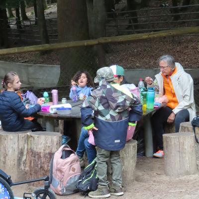 3 Kinder und 2 Erwachsene mit warmen Jacken sitzen im Menschengehege des Wildpark Brettens um einen Tisch und vespern.