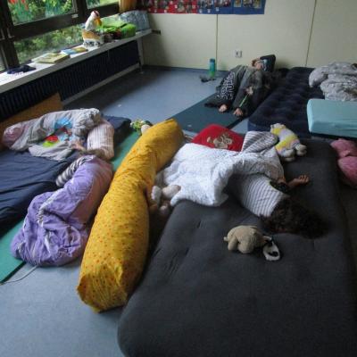 4 schlafende Kinder auf und neben ihren Matratzen im Klassenzimmer.