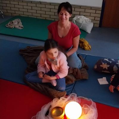 Eine Schülerin sitzt im Schneidersitz. Vor ihr ist eine Leuchtkugel und Klangschale zu sehen.