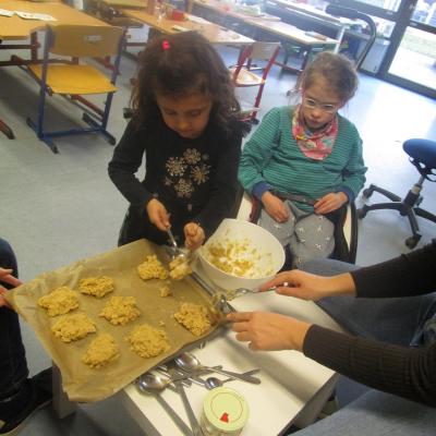 Ein Mädchen setzt im Klassenzimmer Teighäufchen für Scones auf ein Blech, ein anderes schaut zu