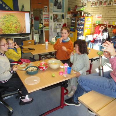 4 Kinder essen im Klassenzimmer Nachos mit Guacamole, im Hintergrund ein Bild von Guacamole auf dem Legamaster