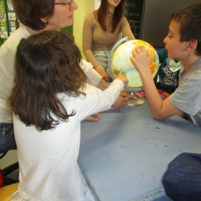 Ein Junge und ein Mädchen suchen Bosnien am beleuchteten Globus, Lehrerin und Erzieherin schauen zu
