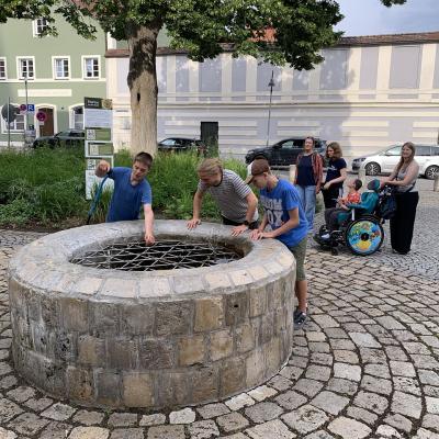 Zwei Schüler und ein Lehrer schauen in einen tiefen Brunnen in Eichstätt.