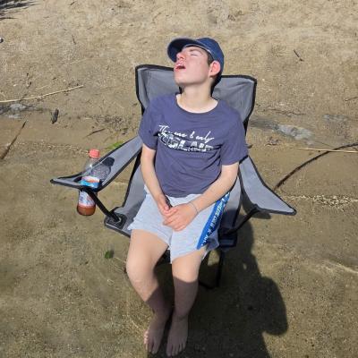 Ein Schüler sitzt auf einem Stuhl im See mit den Füßen im Wasser und genießt den Moment.
