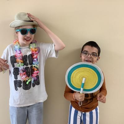 Ein Mädchen und eine Junge schauen in die Kamera. Der Junge hat einen Fächer in der Hand, das Mädchen hat einen Hut und trägt eine Sonnenbrille.