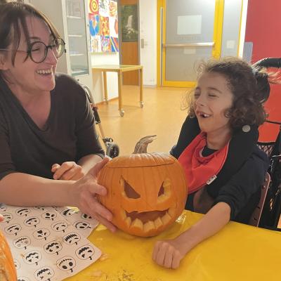 Eine Frau und ein Mädchen lachen in die Kamera und zeigen ihren fertig geschnitzen Kürbis 