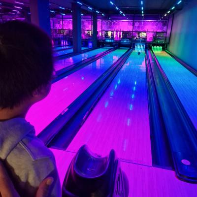 Ein Junge von hinten, der vor einer bunt beleuchteten Bowlingbahn steht.