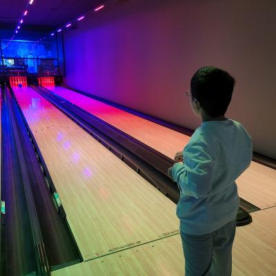 Ein Junge von hinten, der vor einer bunt beleuchteten Bowlingbahn steht.