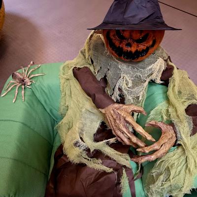Schaurige Halloween Kürbisfigur sitzt auf einem grünen Sessel.